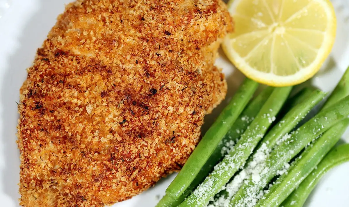 Shake and Bake Chicken on a white plate with a slice of lemon and green beans.