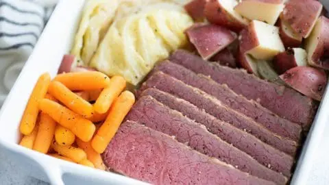 Sous Vide Corned Beef in a white serving dish with carrots, cabbage and red potatoes.