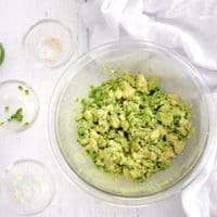 A clean bowl full of 4 ingredients guacamole. Three empty small clear bowls and lime slices are next to the guacamole.
