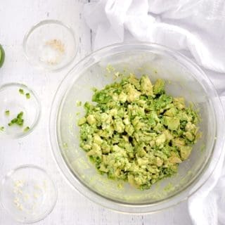 Clean bowl full of 4 ingredient guacamole. 3 empty small clear bowls and lime slices are next to the guacamole.