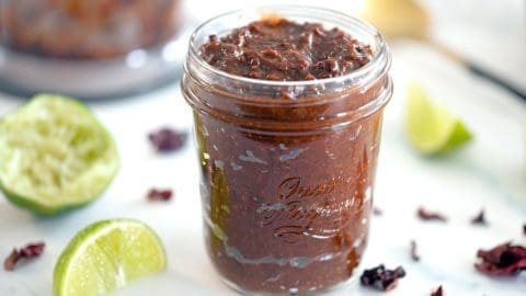 Chamoy sauce in a clear mason jar surrounded by dried hibiscus flowers and lime wedges.