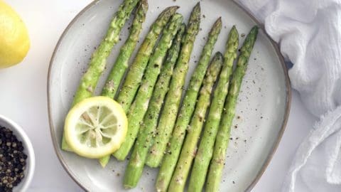 Cream plate with sous vide asparagus and a lemon slice. A whole lemon and dish of black pepper are next to the plate.