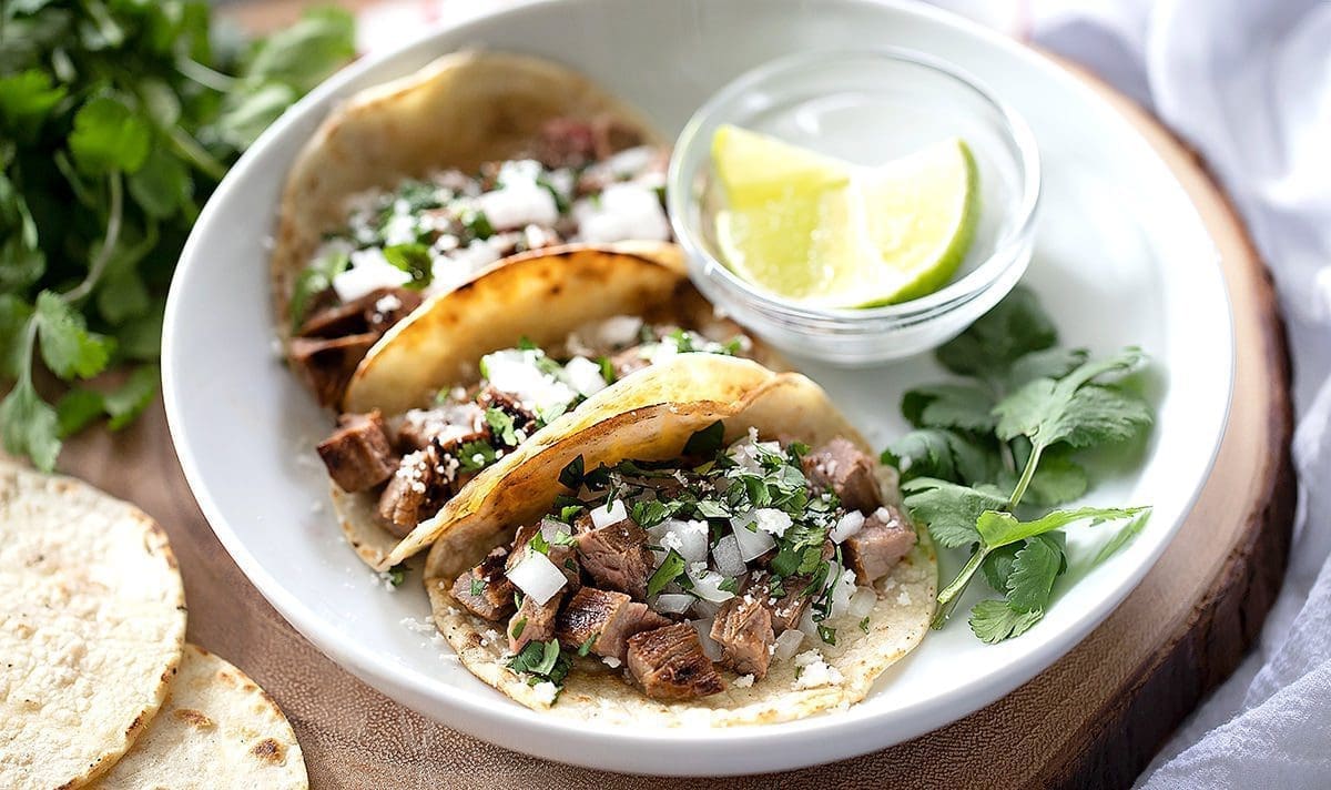 Three carne asada street tacos with lime and cilantro.