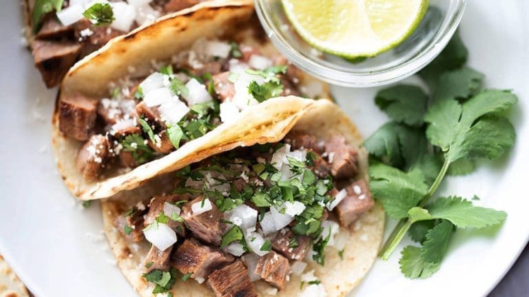carne asada street tacos next to lime and cilantro.