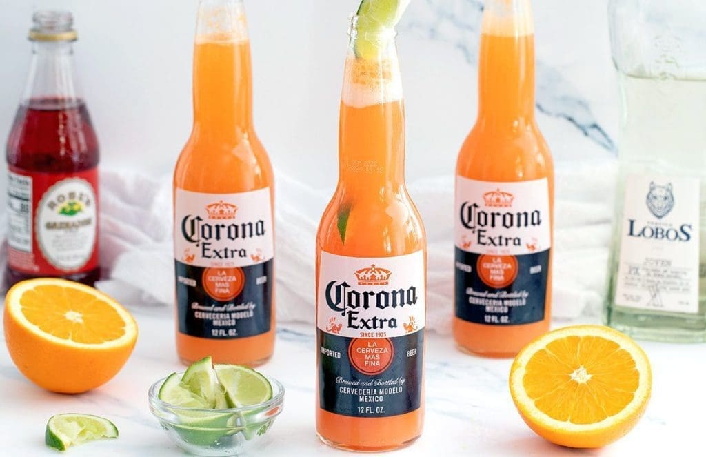 3 Corona Sunset drinks next to oranges and lime.