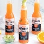3 Corona Sunset drinks next to oranges and lime.