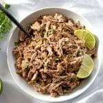Pork carnitas in a white serving bowl topped with lime slices.