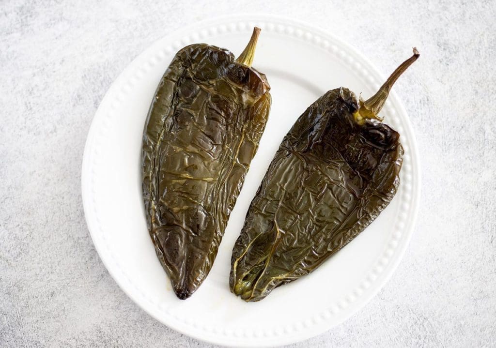 Two roasted poblano peppers on a white plate.