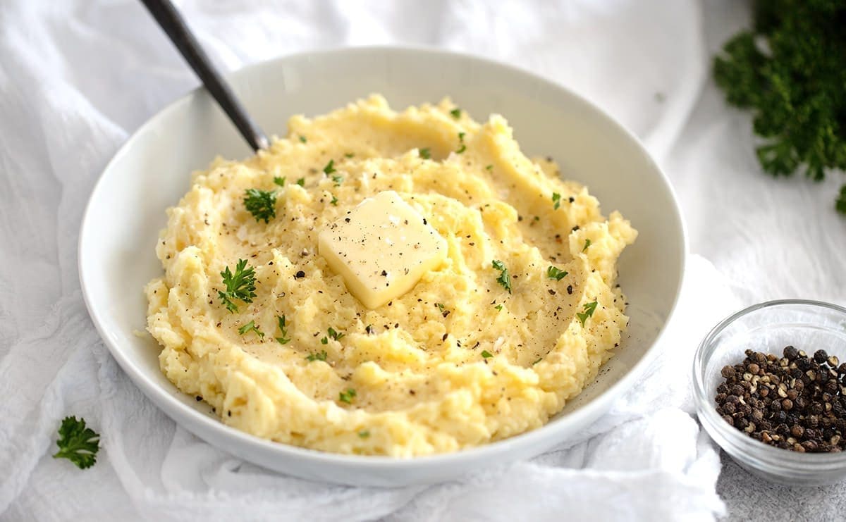 Mashed potatoes in a white bowl next to black pepper and parsley.
