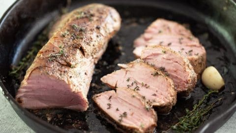 Sliced sous vide pork tenderloin along with thyme and garlic in a black cast iron pan.
