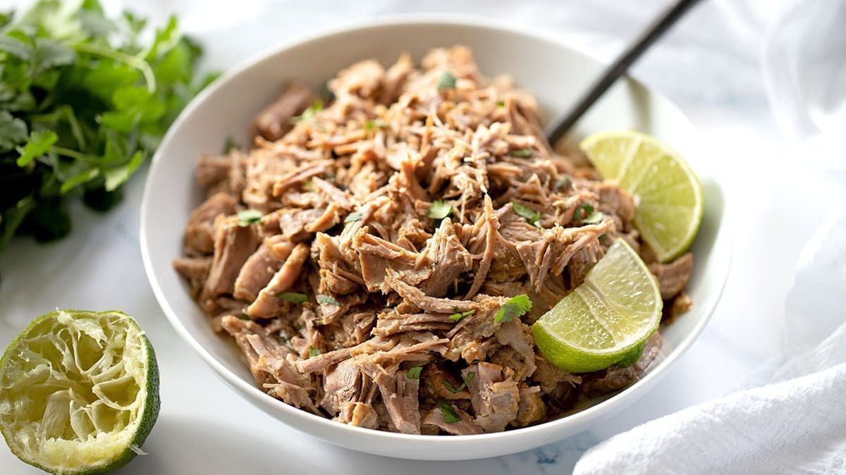 Instant Pot Pork carnitas in a white serving bowl topped with lime slices.