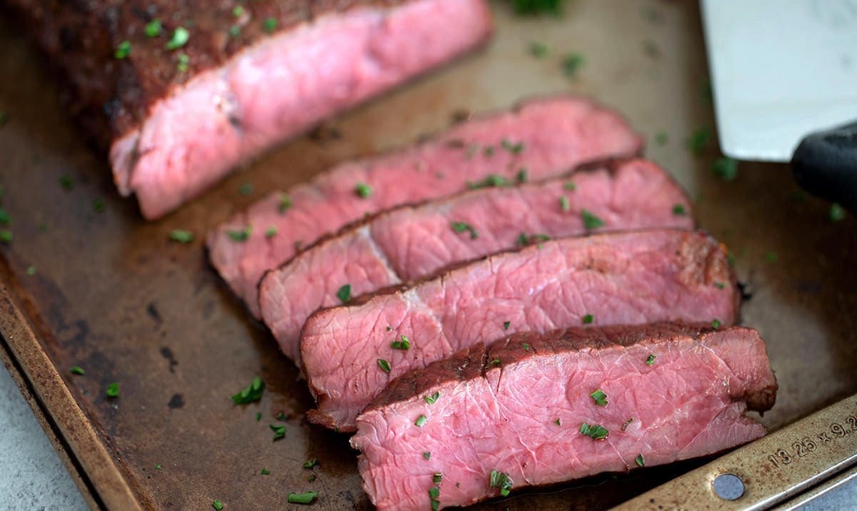 Sliced smoked london broil on a dark baking sheet.