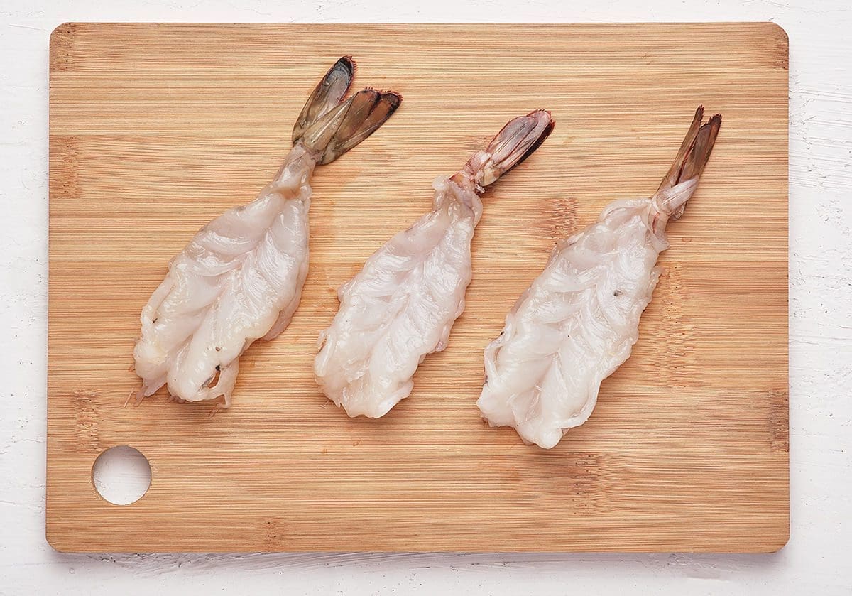 Three butterflied shrimp on a cutting board