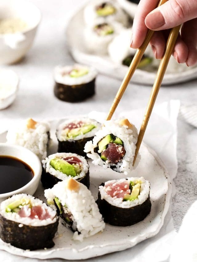 Sushi rolls on a white plate with one being picked up with chop sticks.