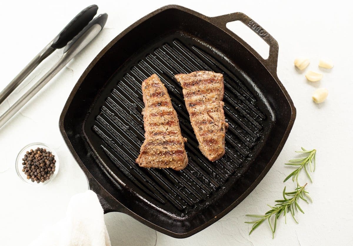 Two pan seared steaks in a cast iron pan.