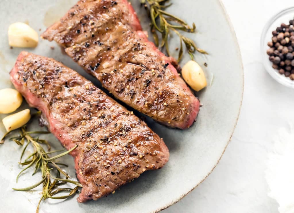 Grilled beef steak next to garlic and rosemary.