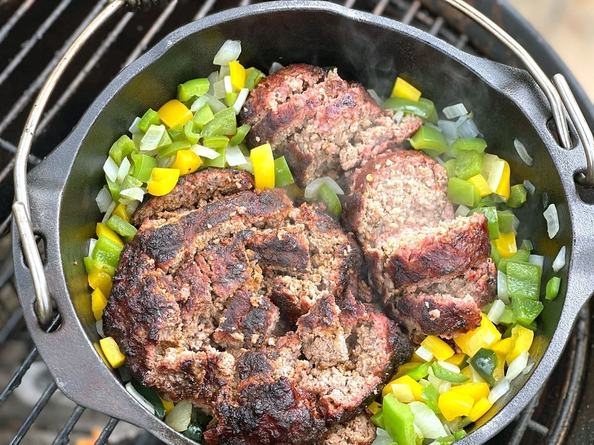Two meat patties in a dutch oven full of vegetables.