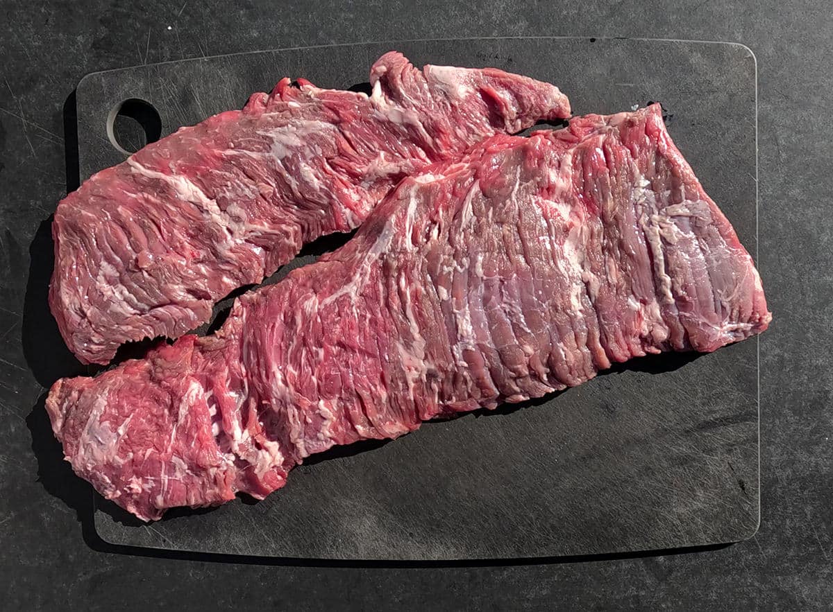 Two cuts of skirt steak on a black cutting board.