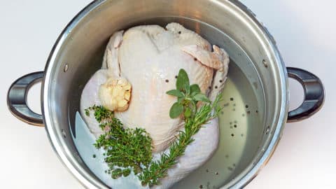 Raw turkey in a stockpot with fresh herbs.