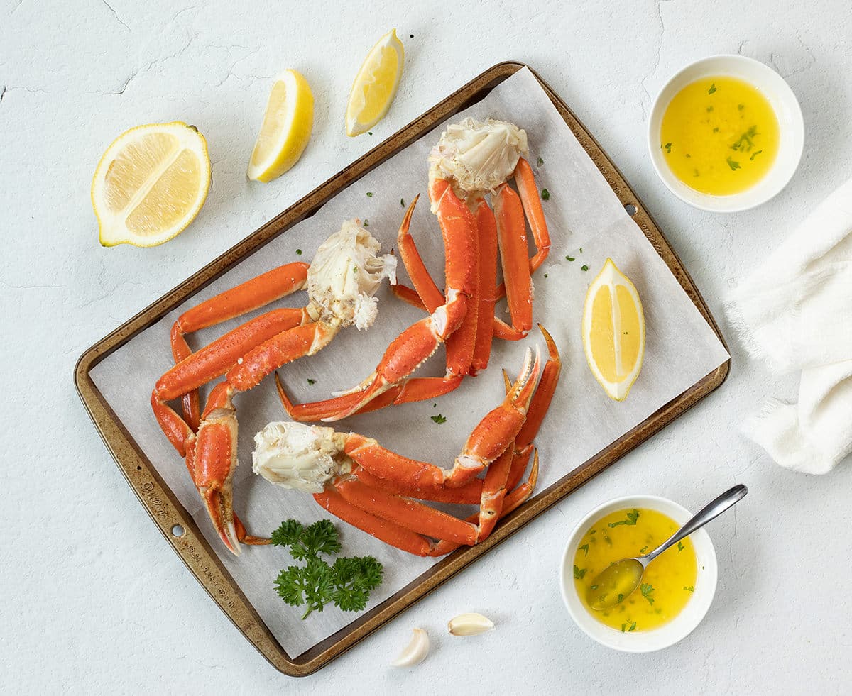 Baked crab legs on a baking sheet with butter and lemon.