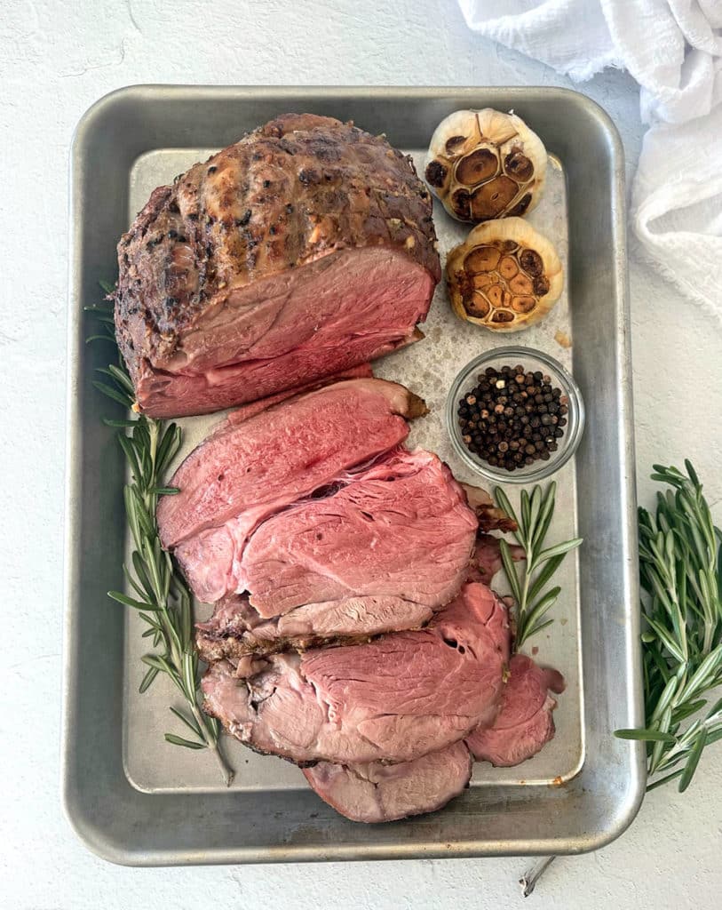 Slow legs of lamb sliced ​​on a silver baking sheet.