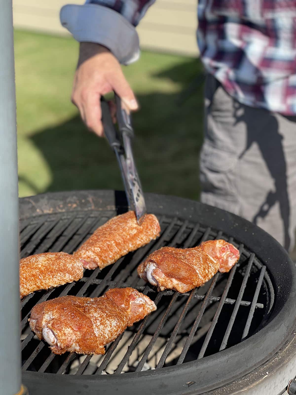 Hang holding tongs putting wings on a grill.