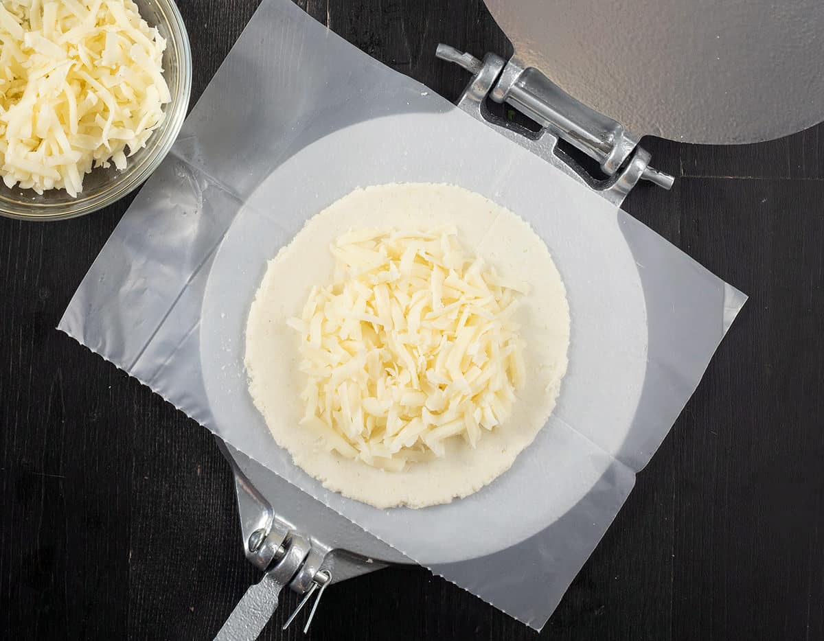 Flattened arepa dough with a mound of cheese on top.