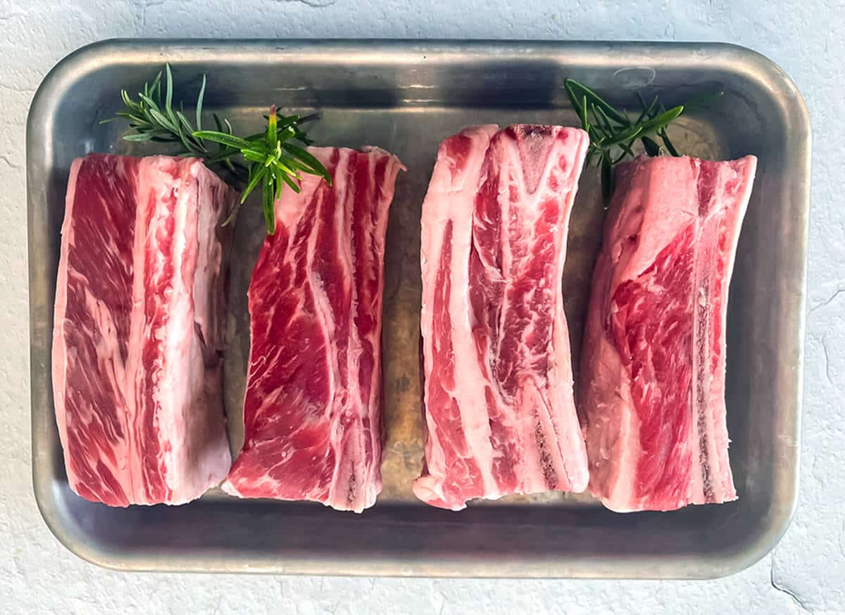 Rare beef ribs on a silver baking sheet.