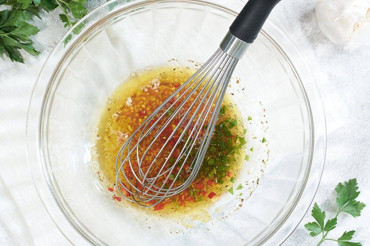 Chimichurri sauce in a clear mixing bowl with a whisk.