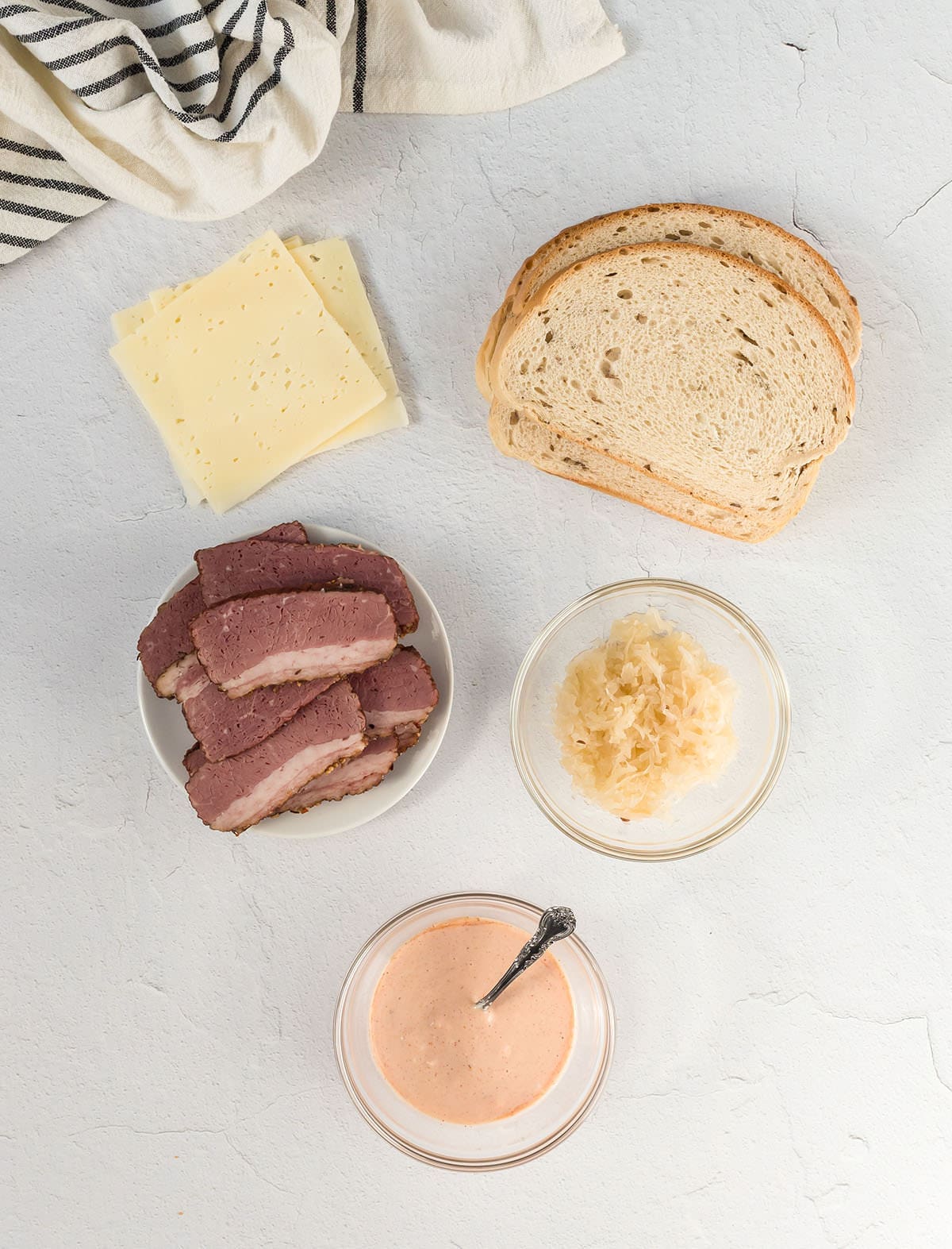 Russian dressing in a clear bowl next to bread, cheese and sliced meat.