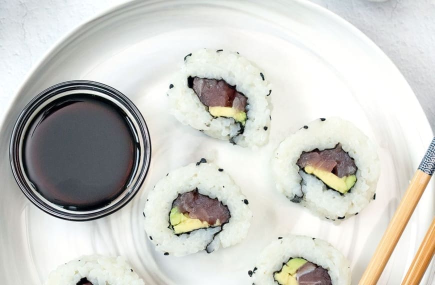 Overhead photo of cut tuna rolls on a white plate with chopsticks.