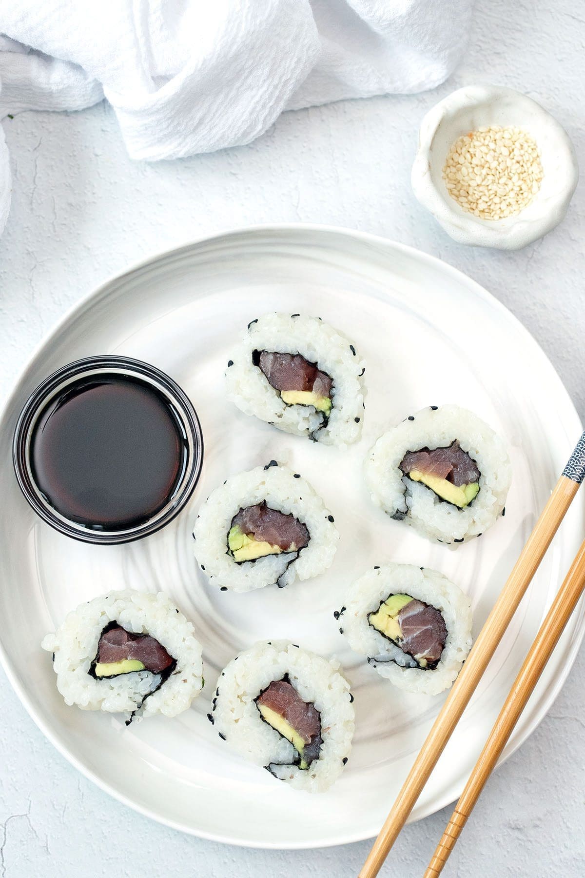 Top view photo of sliced ​​tuna rolls on a white plate with chopsticks.