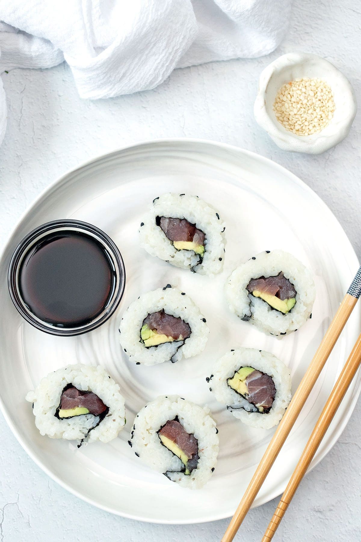 Top view photo of sliced tuna rolls on a white plate with chopsticks.