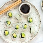 Avocado rolls on a speckled plate with chopsticks.