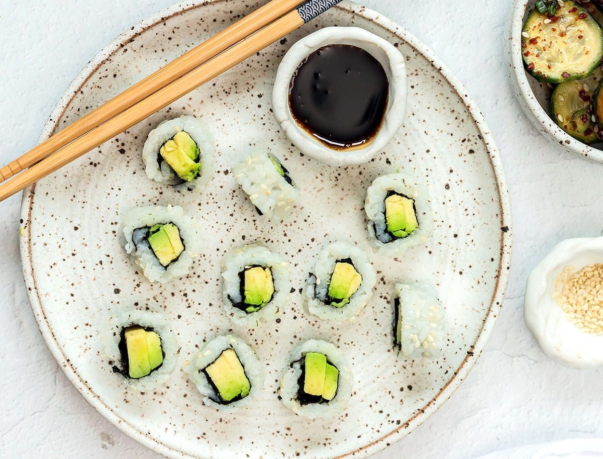 Avocado rolls on a speckled plate with chopsticks.