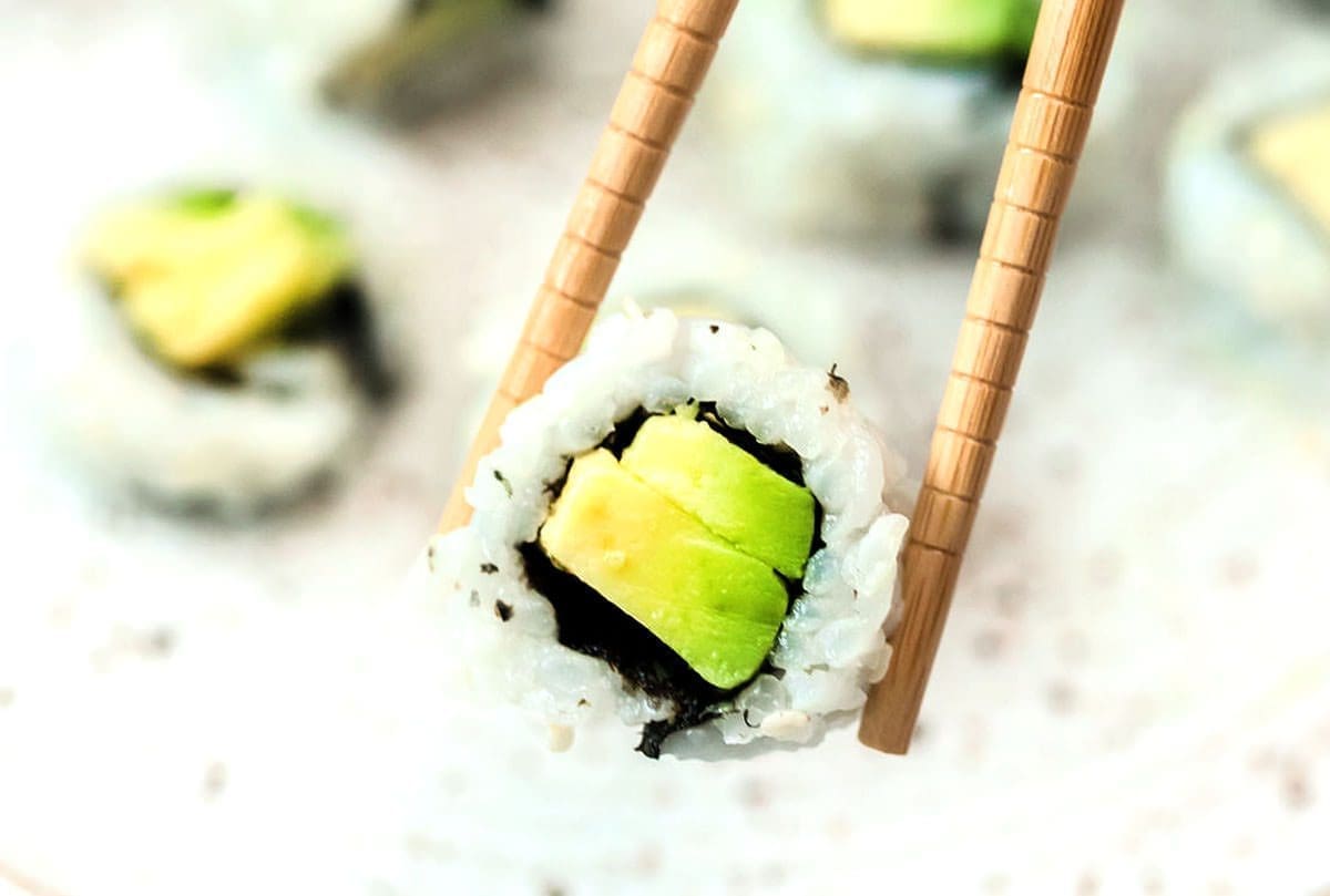 Close up of chopsticks holding a piece of sushi.
