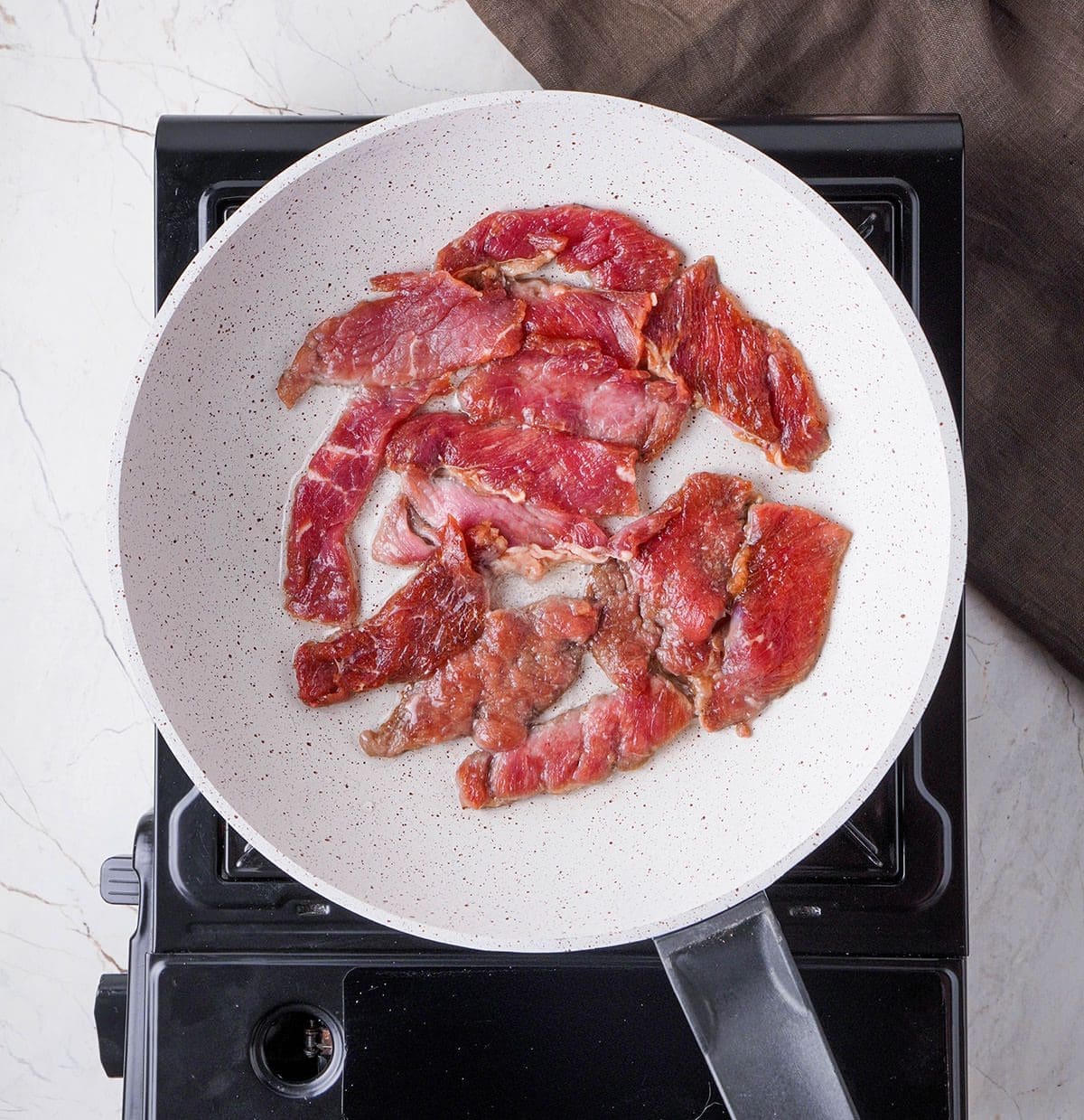 Raw meat strips in a white skillet.