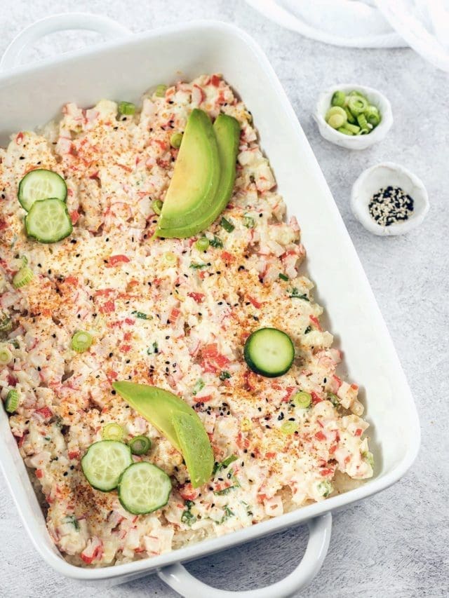 Sushi Bake topped with cucumber and avocados in a white casserole dish.