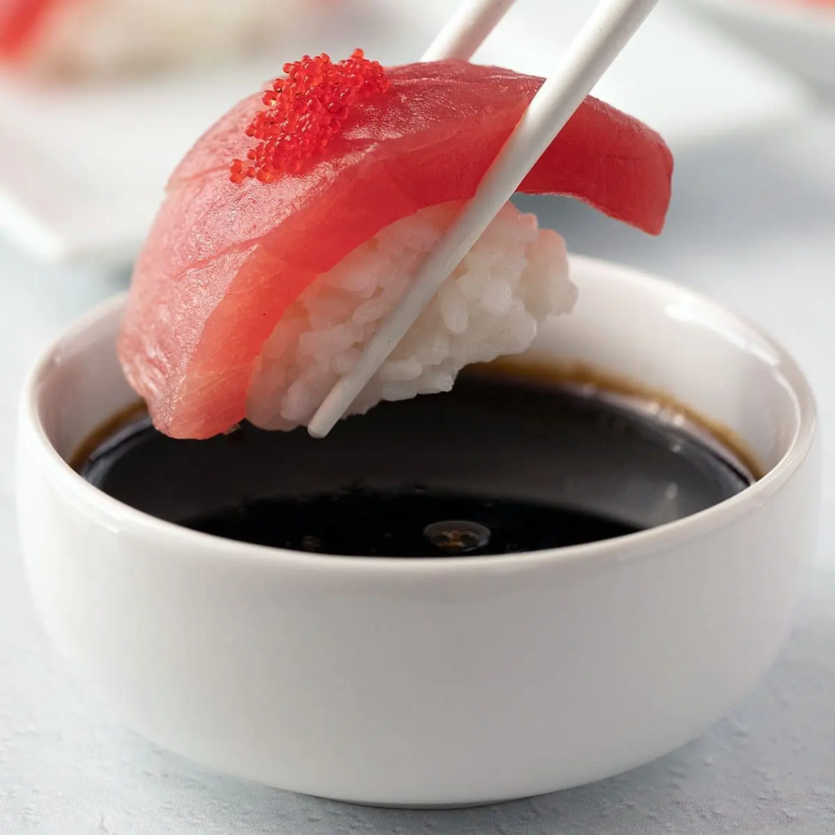 Tuna Nigiri being dipped into a white bowl of eel sauce.