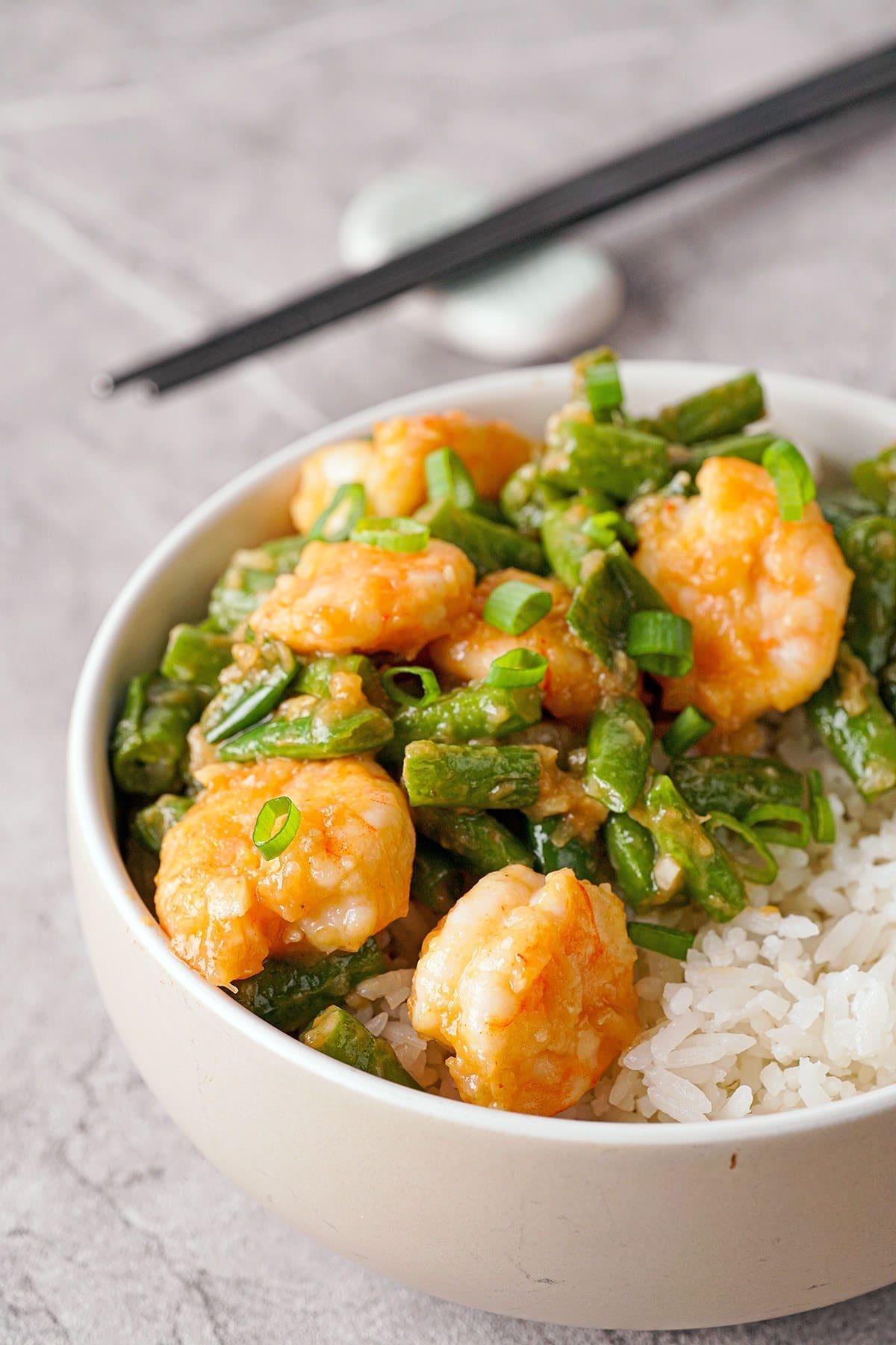 Bowl of spicy shrimp and green beans next to chopsticks.