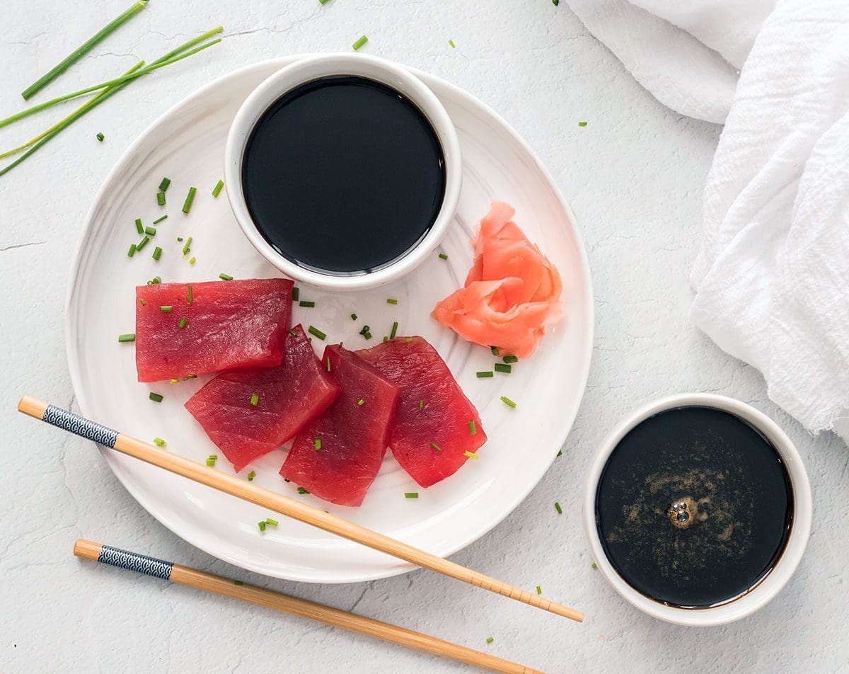 Tuna sashimi on a plate with chopsticks and eel sauce.