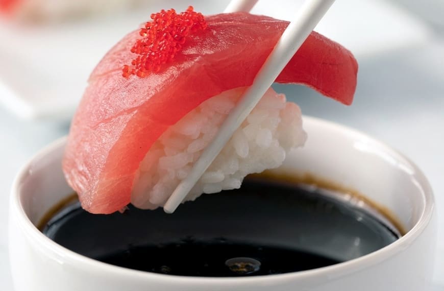 Tuna nigiri being dipped in sushi sauce.