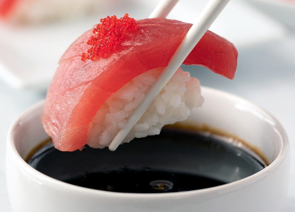 Tuna nigiri being dipped in sushi sauce.