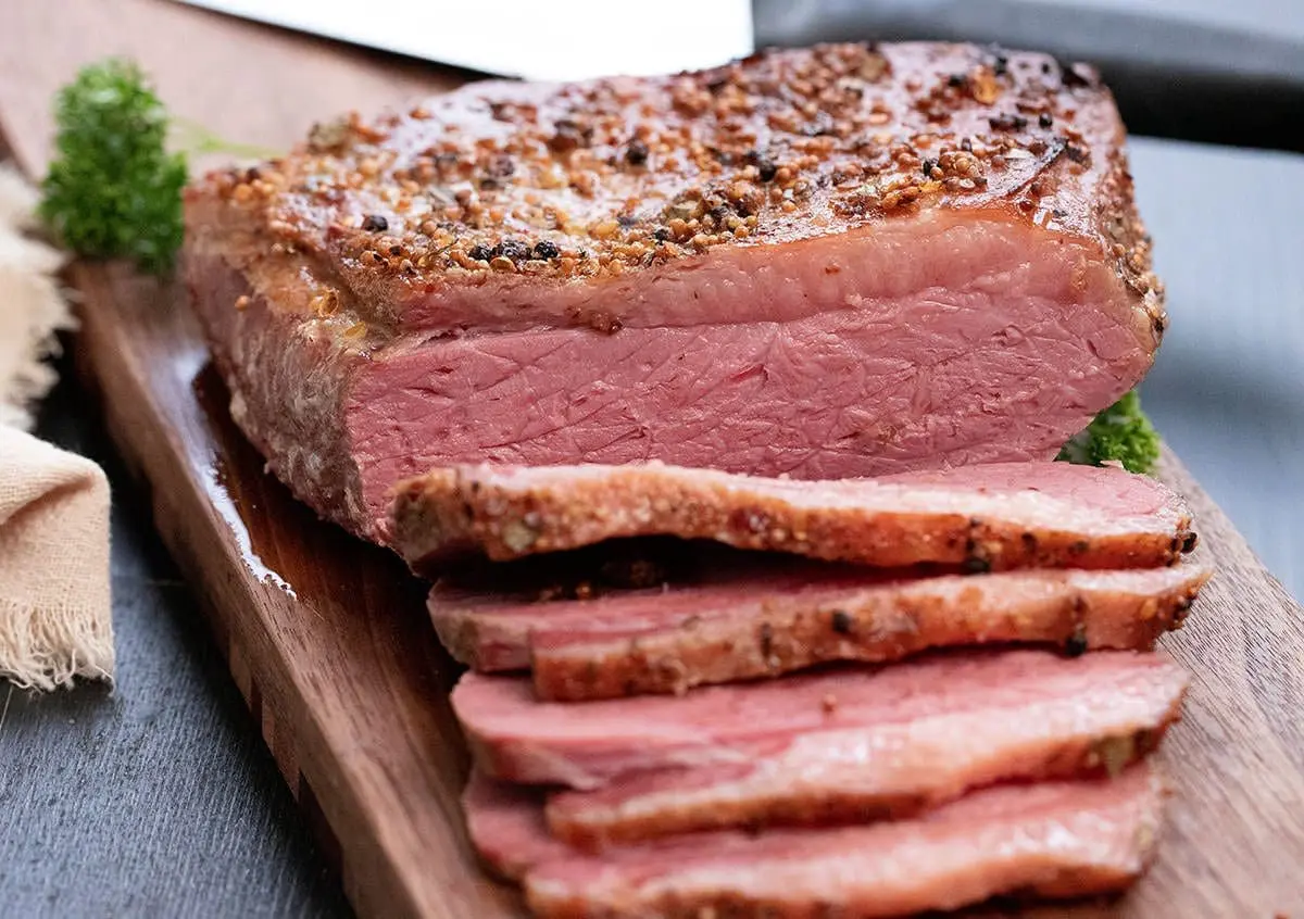 sliced baked corned beef on a brown cutting board.