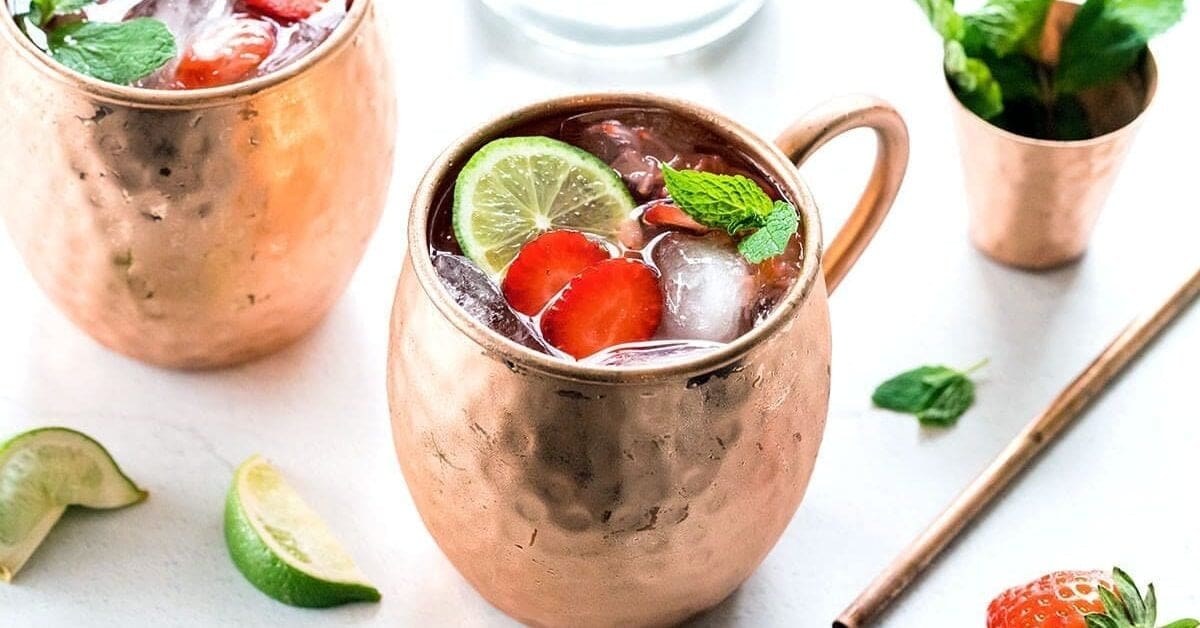 Three copper mugs full of strawberry mules garnished with mint leaves.
