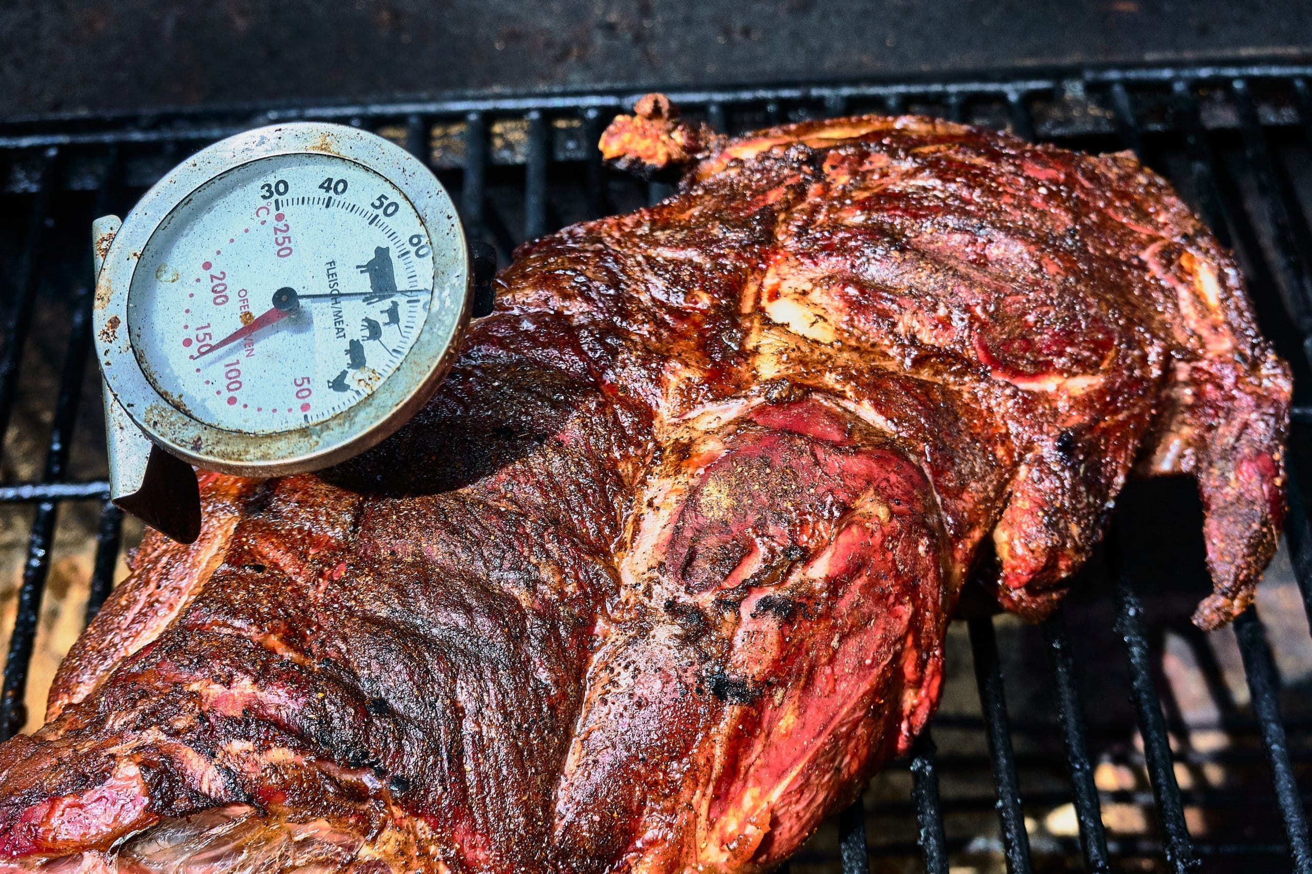Meat roast on the grill with a thermometer inserted in it.
