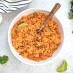 Mexican rice in a white bowl with a wooden spoon.