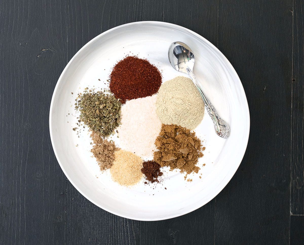 Individual spices on a white plate with a silver spoon.