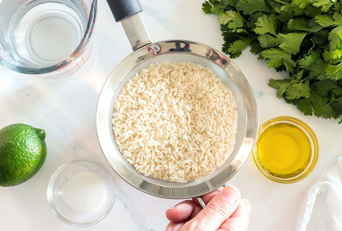 Rice in a silver sieve next to a variety of ingredients.