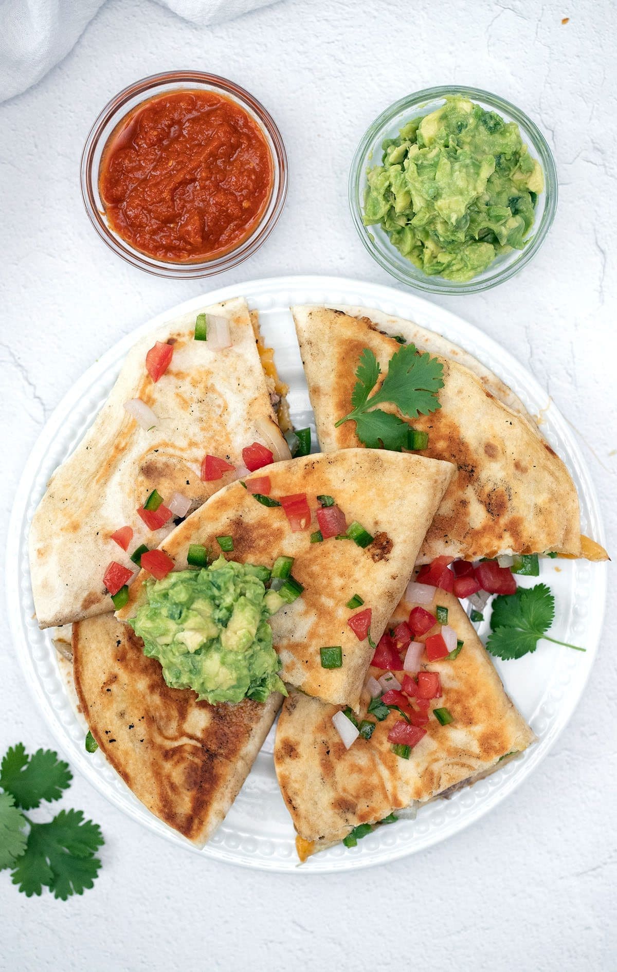 Quesadilla with steak on a white plate with salsa and quacamole.